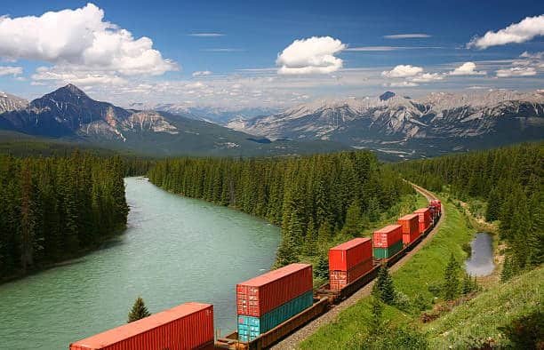 Freight train carrying shipping containers through the Canadian Rockies mountains along a river