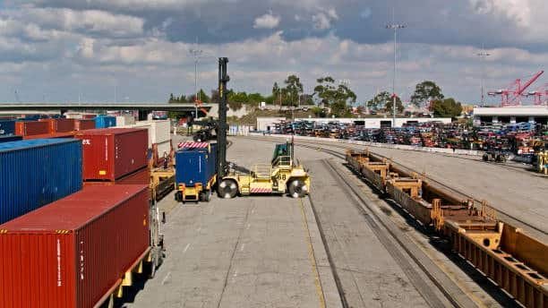 Forklift moving shipping containers inside an international freight yard.