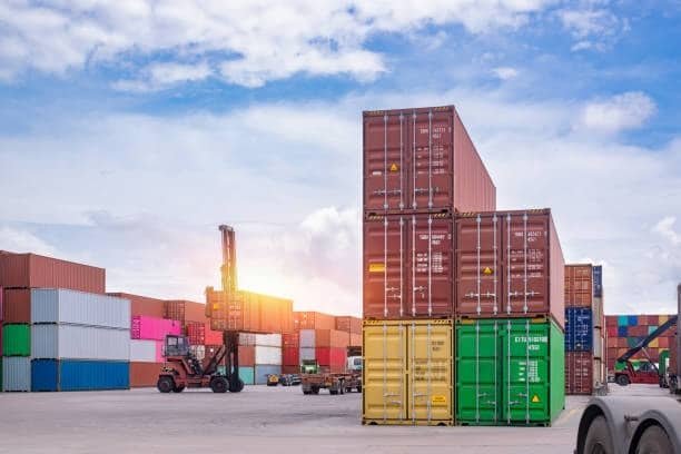 Forklift moving shipping containers at sunrise in a large container depot.