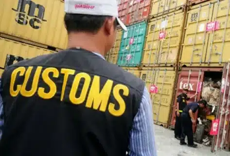 Customs official in safety vest overseeing forklift operations in a container yard for import customs clearance