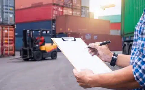 Customs officer in CUSTOMS vest standing at open shipping container during import clearance inspection