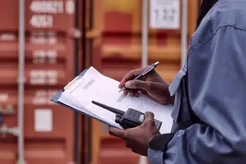 Customs officers in CUSTOMS uniforms supervising unloading and clearance of imported boxes from container