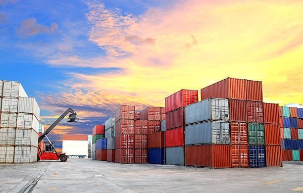 Stacked shipping containers at sunset in a logistics yard prepared for ground transportation.