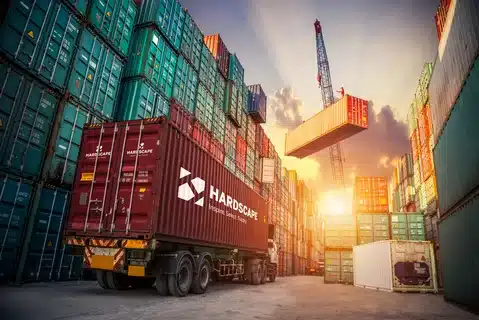 Logistics worker checking stacked shipping containers, representing safety and efficiency in ground shipping operations.