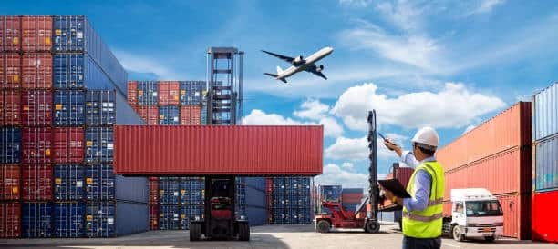 Worker supervising cargo containers with airplane flying above in logistics hub.