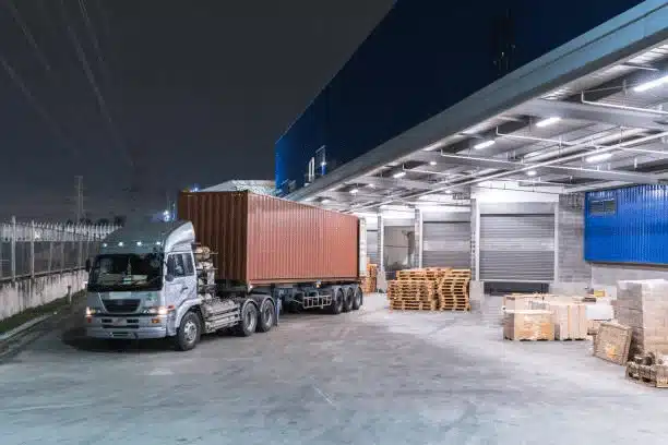 Logistics truck loading cargo container at warehouse facility for shipping.