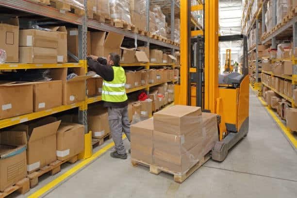 Employee organizing boxes in fulfillment warehouse with forklift.