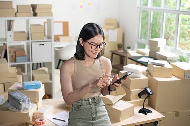 dropshipping business owner checking orders on mobile phone in packaging room