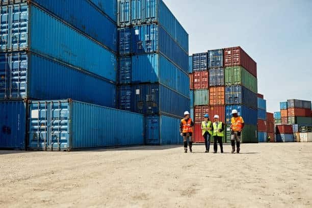 Workers wearing safety gear walking near stacked containers, representing inspection and handling in LCL shipping.