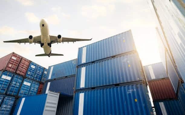 Airplane flying over stacked shipping containers, symbolizing global air freight logistics and international transportation networks.