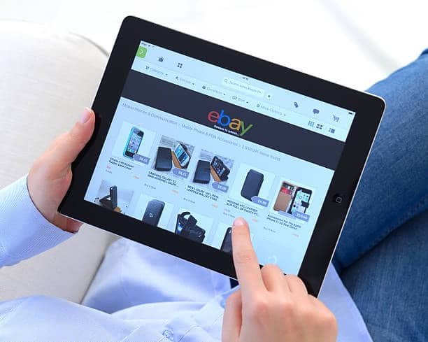 Person using a tablet to browse eBay product pages, representing customer expectations for shipping and delivery.