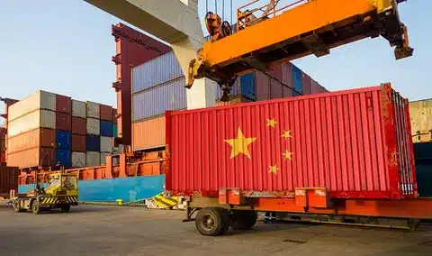 Red container with China flag being lifted at a shipping port, preparing for export to Switzerland.