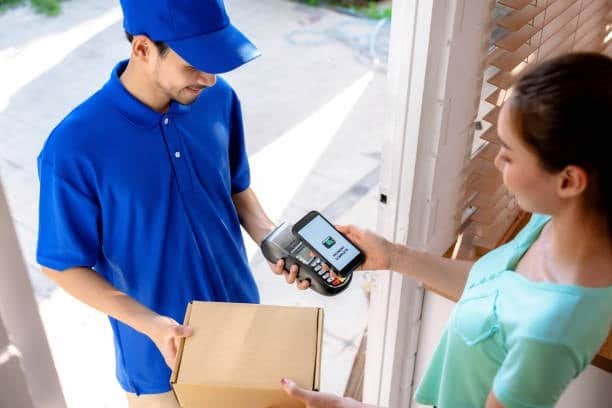 Courier using a handheld device to confirm delivery and payment at the customer’s door.