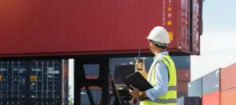 A customs clearance officer using a walkie-talkie while inspecting a shipping container at the port.
