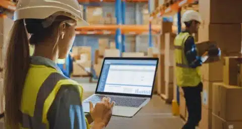 Fulfillment center worker using laptop to manage inventory and logistics.