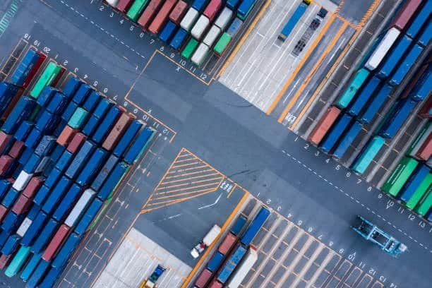Port scene with cargo ships and stacked containers demonstrating how freight transitions from sea transport to ground shipping.