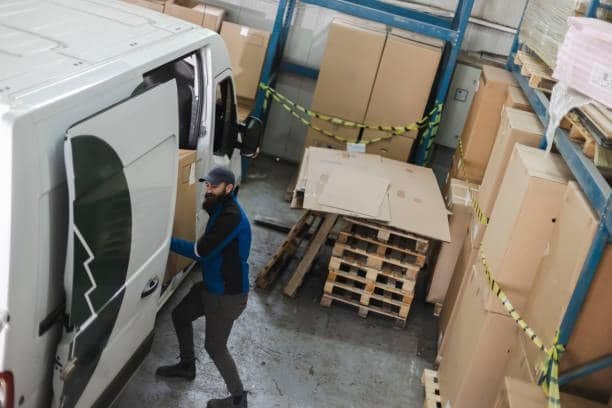 Delivery courier standing beside a van full of packages for door-to-door transport.