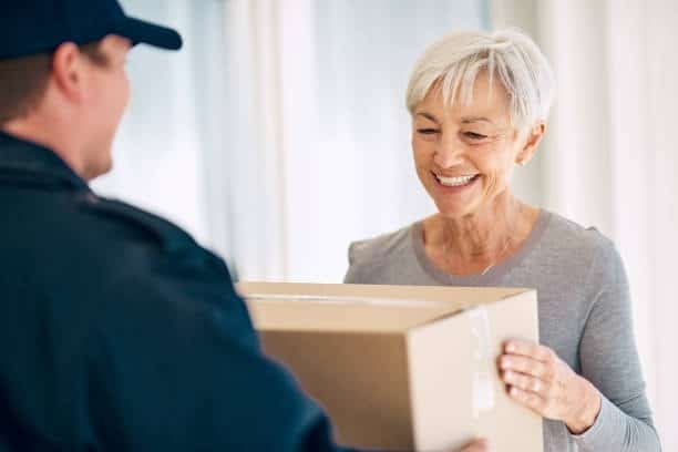 Senior woman receiving package from door to door delivery service.