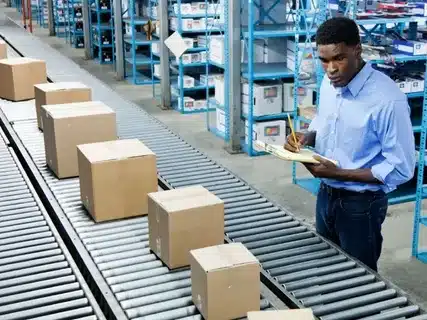 Fulfillment center employee inspecting packages on conveyor for quality control.