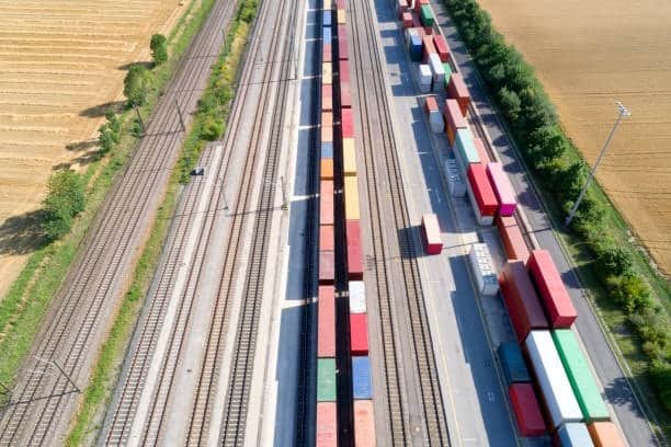 Aerial view of rail freight transport terminal with intermodal containers, representing the integration of logistics and transportation networks.