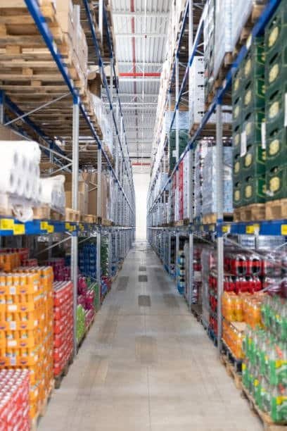 Warehouse aisle filled with stacked goods and large boxes for big box shipping and inventory storage.