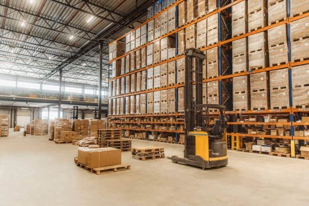 Modern warehouse interior with forklift moving pallets and goods, illustrating logistics storage and inventory management operations.