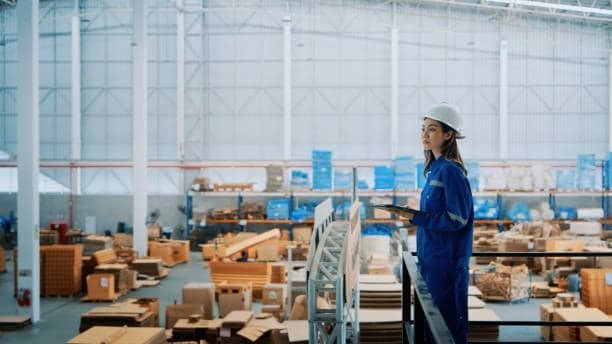 Female warehouse worker in protective gear inspecting goods in a distribution facility.