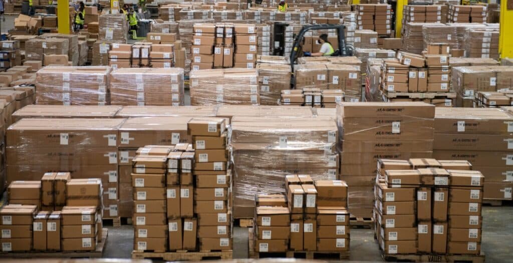 Stacks of packaged apparel boxes in a 3PL warehouse with workers managing shipments and inventory.