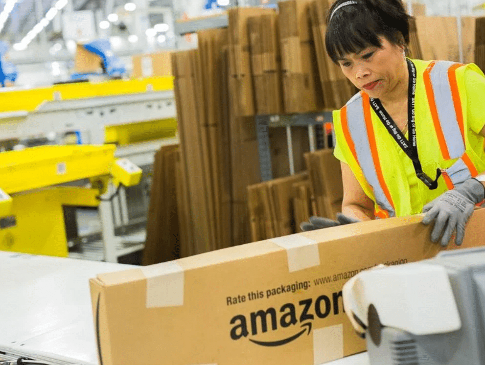 Warehouse employee packaging apparel items in Amazon-branded boxes for FBA shipment.