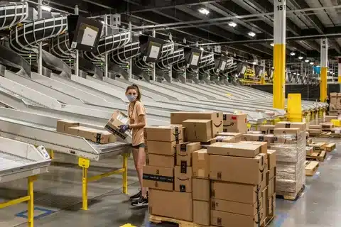 Worker sorting and scanning apparel boxes in an Amazon FBA fulfillment center.