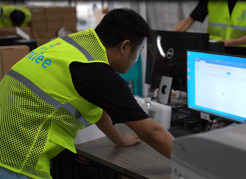 A BM Supply Chain warehouse employee monitoring the digital fulfillment system on a computer to track orders and inventory in real time.