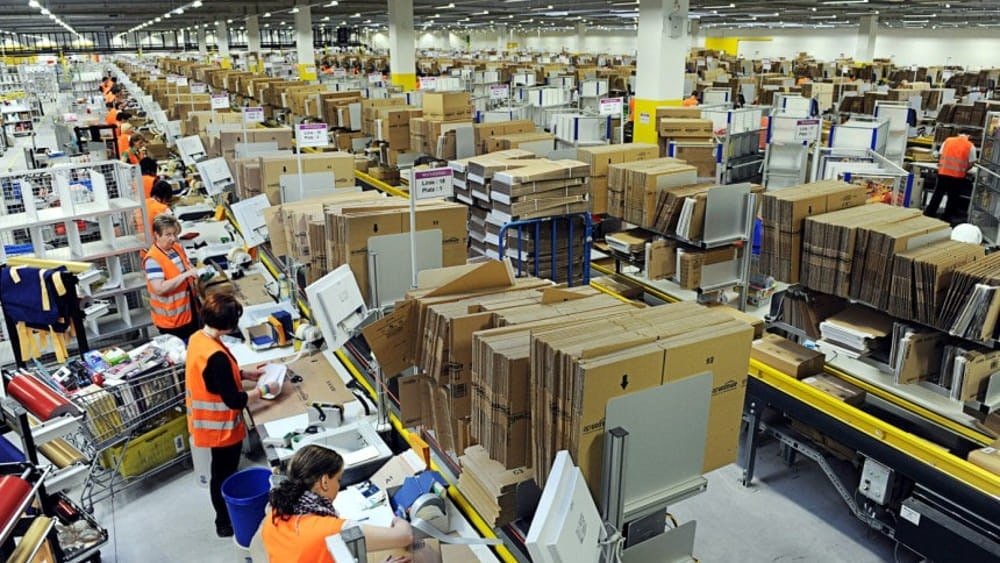 Workers processing and packing apparel orders at a fulfillment center, preparing packages for shipping.
