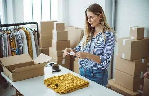 Woman packing apparel items into a box in a warehouse for online order fulfillment, preparing them for shipment.