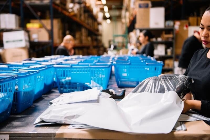 Warehouse employee packing apparel items into shipping bags for e-commerce order fulfillment.