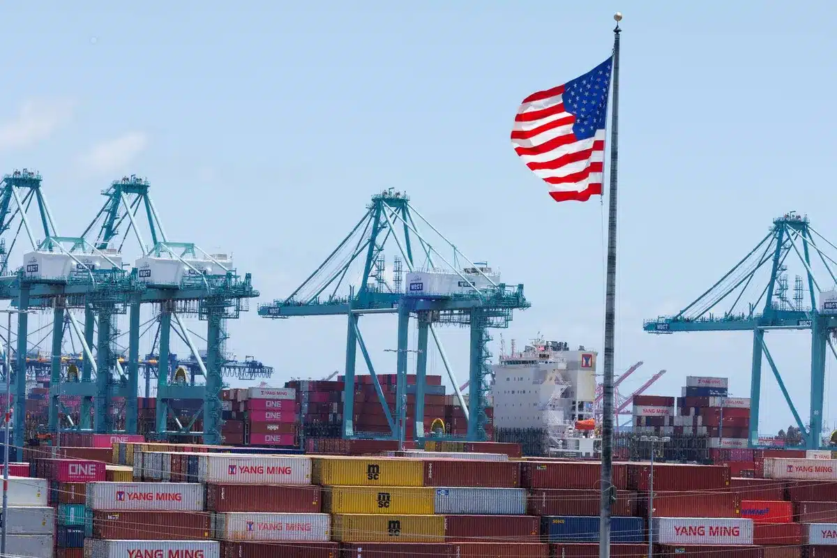 A U.S. port with cranes, shipping containers, and an American flag, illustrating the real cost of importing to the U.S. in 2025, including duties and taxes.