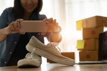 Woman taking product photo of shoes for AliExpress store listing.