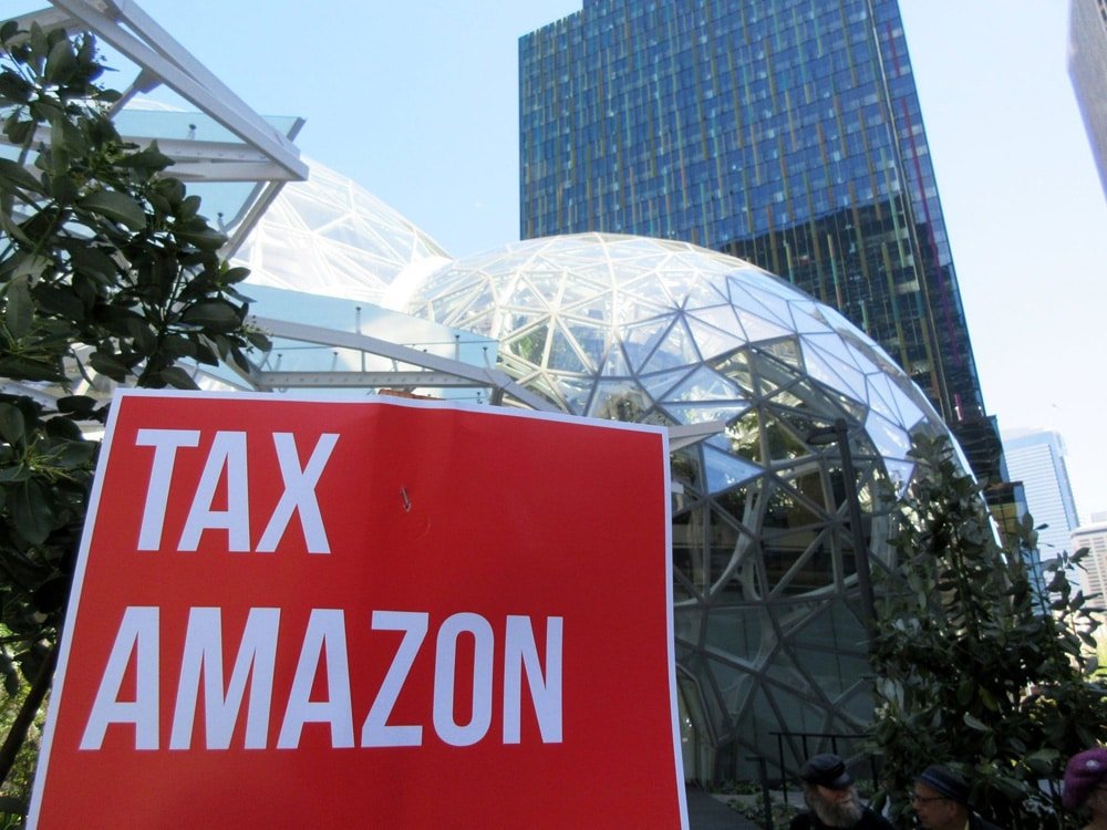 A protest sign reading "TAX AMAZON" in front of Amazon's headquarters, symbolizing the importance of duty optimization for Amazon sellers to reduce import costs in 2025.