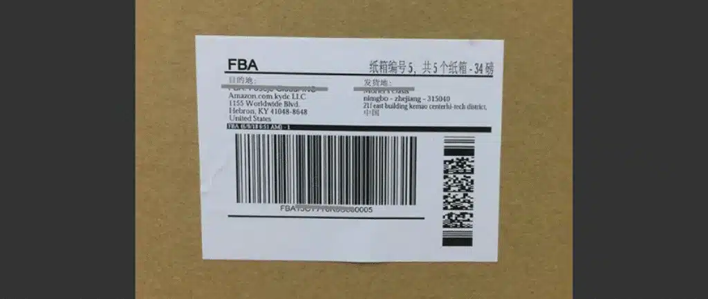 Amazon FBA carton label attached to a brown shipping box, showing required barcode and address details.