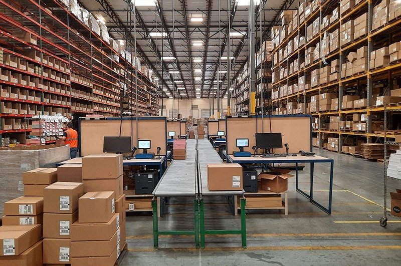 Warehouse fulfillment center with conveyor systems and packing stations, showcasing BM Supply Chain’s efficient order processing and pick–pack services.