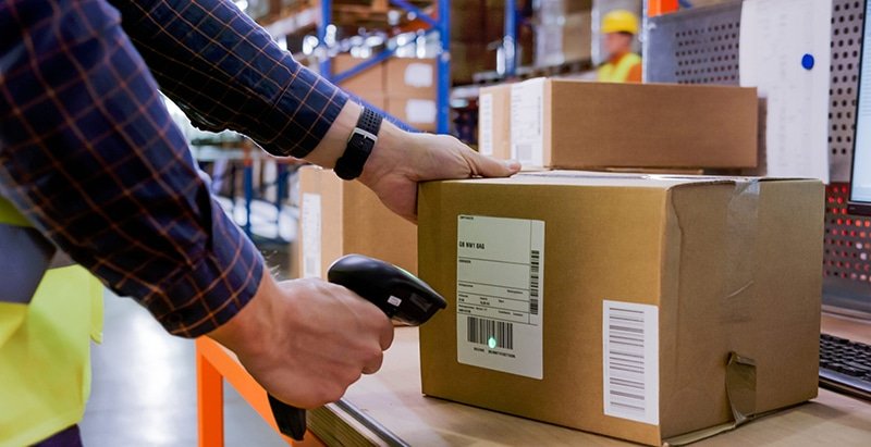Warehouse staff scanning a carton label using a barcode scanner, demonstrating automated receiving and accuracy assurance in B2B fulfillment.