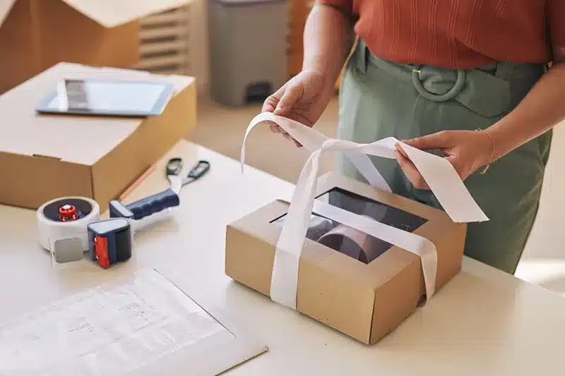 Hands preparing a custom package with ribbon and kraft box, representing personalized packaging solutions in B2B fulfillment operations.