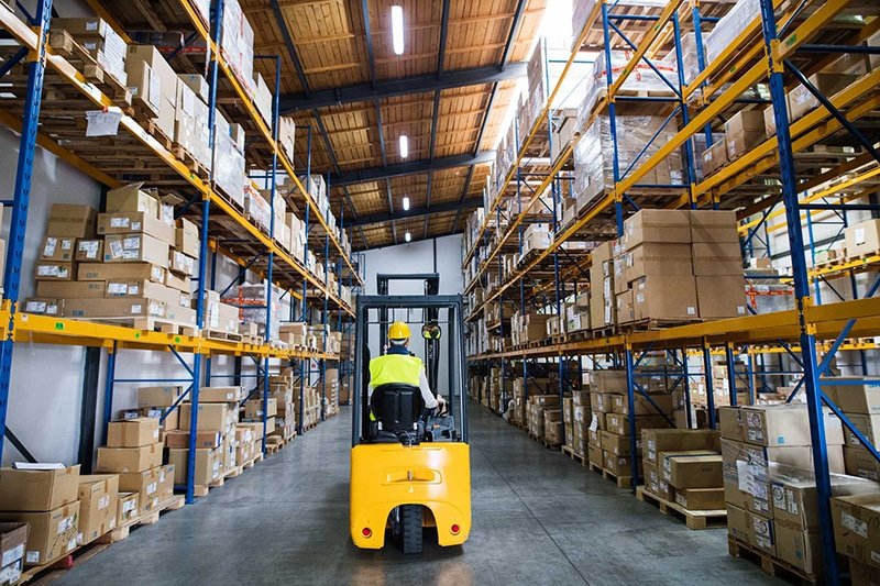 A forklift operator moving pallets in a warehouse, representing efficient logistics workflows within B2B fulfillment operations.