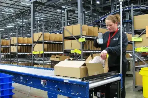 Warehouse employee inspecting and packing returned products on a conveyor line as part of the ecommerce returns process.