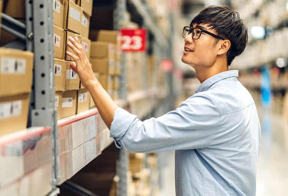 A warehouse staff member checking items on a shelf, representing inventory accuracy and stock management in B2B fulfillment operations.