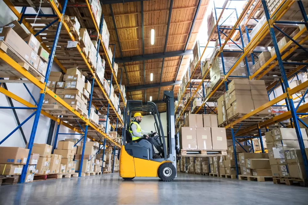Warehouse worker operating a forklift to move pallets of cartons inside a large B2B fulfillment center