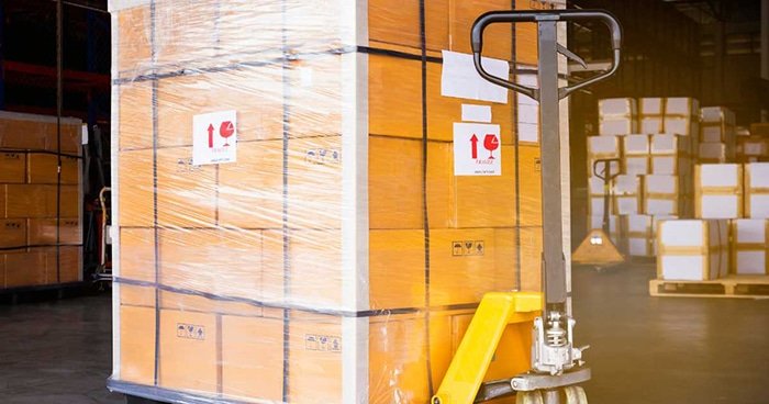 Palletized cartons wrapped for protection being moved with a pallet jack inside a warehouse during B2B fulfillment operations