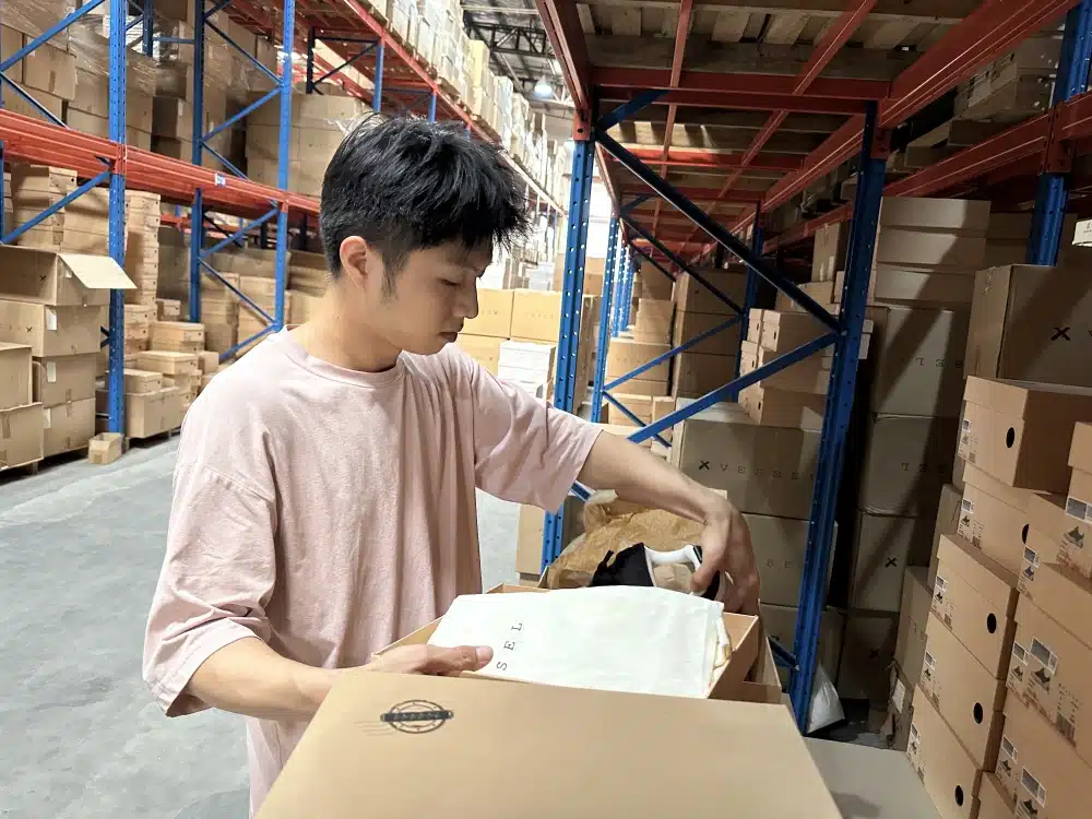 Warehouse worker inspecting footwear inside an open shoebox during ecommerce fulfillment checks