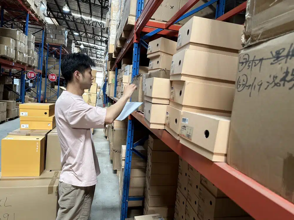 Warehouse worker scanning barcodes on stacked shoeboxes during inventory verification in China