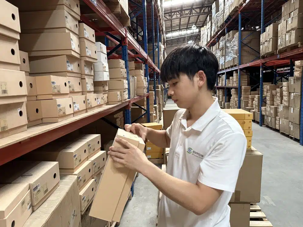 Warehouse employee checking a shoebox label beside stocked racks in a China fulfillment center