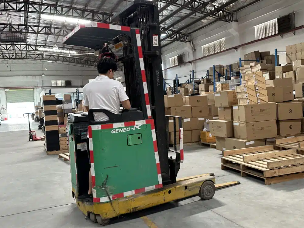 Forklift operator beside stacked cartons and wooden pallets in a China 3PL warehouse